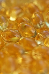 A macro shot shows a heap of shiny, golden Omega-3 fish oil softgel capsules. Concept of: Health.