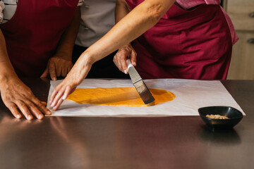 Pastry chefs spreading yellow mixture on baking paper during cooking course