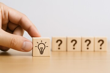 Creative problem-solving concept: Hand placing a lightbulb block among question marks on a wooden surface.