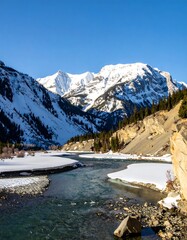 A wintry river winding through a snow-capped mountain valley, showcasing the beauty of nature's tranquil landscape.