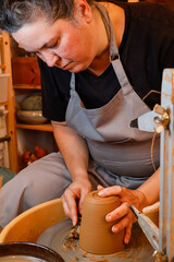 Obraz premium Pottery woman works with clay on a potter's wheel. Making pottery. Small business. Authentic workshop in the background