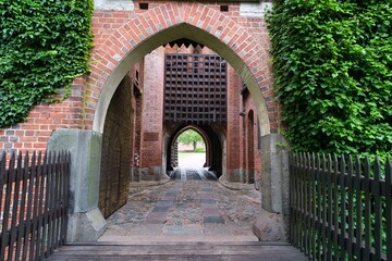 Fototapeta premium Beautiful historic brick archway leading to a serene courtyard in a medieval castle during a sunny day