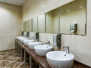 The public restroom is designed with a long row of sinks each paired with mirrors, creating a crucial area for personal care and hygiene within a shared facility for users