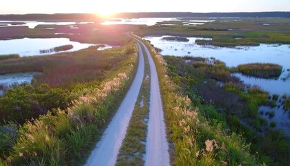 A gravel path winds through a tranquil wetland at sunset, showcasing vibrant colors and serene natural beauty.