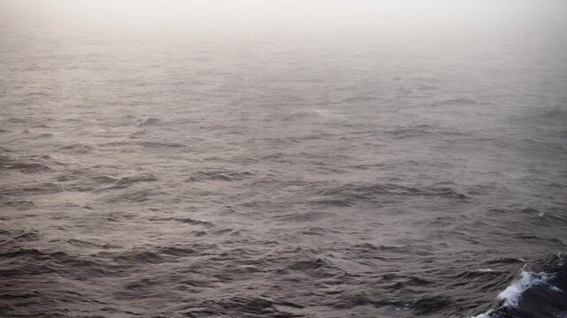 Foggy ocean surface with gentle rolling waves fading into a hazy horizon, capturing a quiet, overcast seascape where mist softens texture and reduces visibility across open water.