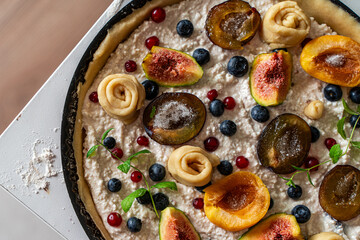 Raw tart or open summer pie with figs, prunes, apricots and blueberries is ready to bake in a round mold. Close-up. View from above. High quality photo