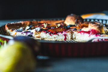 A delicious berry dessert, a piece of tart or an open sweet pie with figs, blueberries and apricots on a black plate. High quality photo