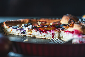 A delicious berry dessert, a piece of tart or an open sweet pie with figs, blueberries and apricots on a black plate. High quality photo
