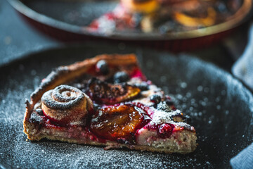 A delicious berry dessert, a piece of tart or an open sweet pie with figs, blueberries and apricots on a black plate. High quality photo