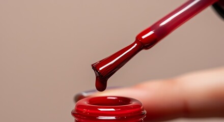 Macro close-up of nail polish brush with falling crimson drop and manicured fingernail in studio lighting