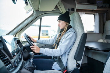 Young woman with braids wearing beanie and hoodie, sitting in the driver’s seat of a campervan and looking forward calmly before departing on a peaceful road trip through the Scottish countryside