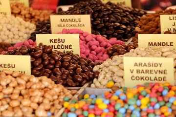Colorful candy stall with assorted nuts in chocolate, caramel, and sugar coating, offering festive sweets, crunchy snacks, and traditional confectionery at a market.