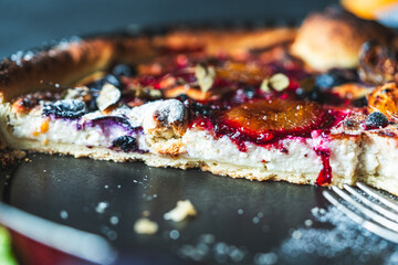 A delicious berry dessert, a piece of tart or an open sweet pie with figs, blueberries and apricots on a black plate. High quality photo
