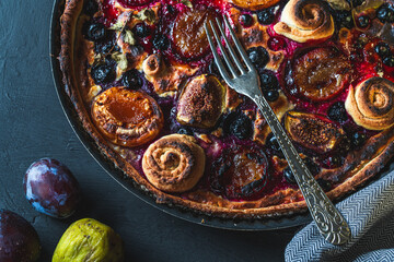 A tart or open pie with blueberries, figs, prunes and apricots in a baking dish on a gray background with a fork and napkin on the table. Top view. High quality photo