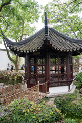 Decorative gazebo or pavilion in oriental style in green area between trees and bushes in Humble Administrator's Garden, classical Chinese garden, Suzhou, Jiangsu, Gusu District, China. Vertical image