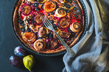 A tart or open pie with blueberries, figs, prunes and apricots in a baking dish on a gray background with a fork and napkin on the table. Top view. High quality photo
