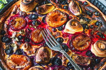 A tart or open pie with blueberries, figs, prunes and apricots in a baking dish on a gray background with a fork. High quality photo