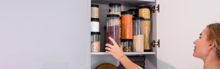 Organized kitchen pantry with cylindrical plastic jar for storing loose products,  in grey tones. banner
