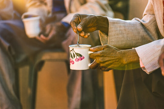 old african man , close up on hand, drinking tea, kgotla meeting the community drinking tea in the yard outdoors, stirring the beverage with a spoon