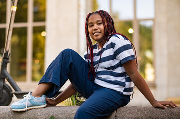 Smiling cute girl in striped tshirt resting after a ride on a scooter