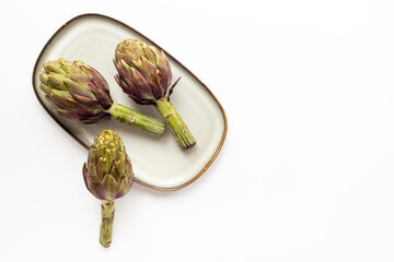 Tree heads of purple artichokes on a plate top view. Vegetables food ready to cook