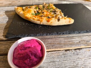 delicious slice of pizza lies on a black granite board. Various sauces are nearby