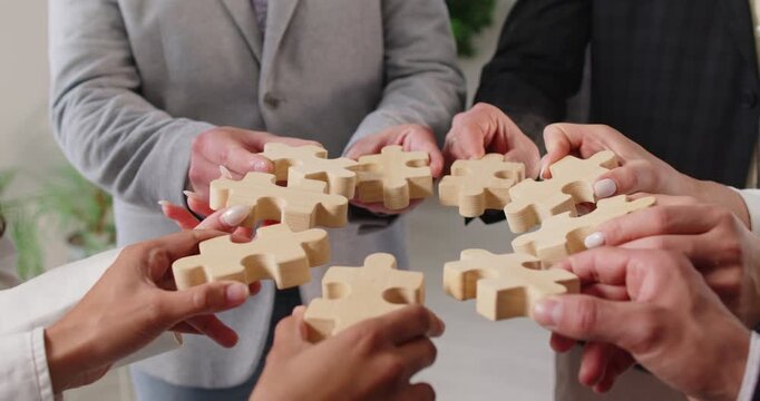 Unknown business people standing in circle, holding wooden puzzle pieces, working as team, collaborate for solving problem, finding idea or solution during meeting. Team building activity