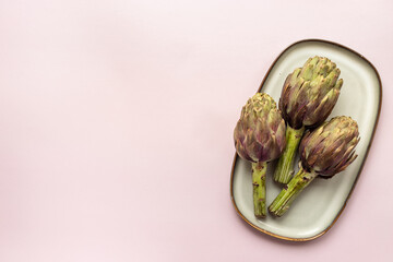 Tree heads of purple artichokes on a plate top view. Vegetables food ready to cook
