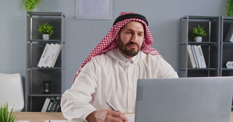 Focused arab businessman conducts online video call, working with laptop in office, enhancing communication and meeting conversation, fostering business engagement in a professional workspace. - Powered by Adobe
