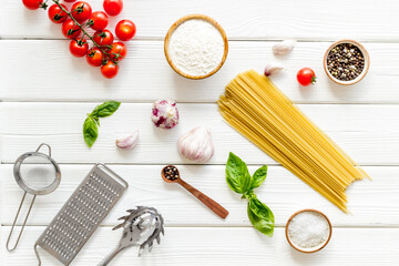 Flat lay of uncooked spaghetti with ingredients for cooking Italian pasta - tomatoes and basil with garlic - on a white wooden background, top view