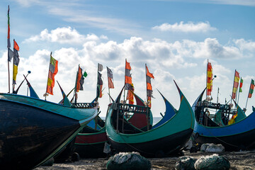 Obraz premium Fishing boats at the beach with colorful flags under a cloudy sky. Colorful Wooden Fishing Boat On a Cox's Bazar Sea Beach, Bangladesh With Blue Sky Background. 
