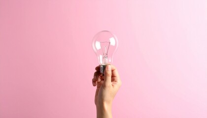 Hand holding clear light bulb against pink background.