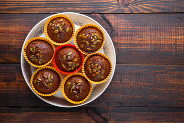 Autumn pumpkin cupcakes or baked muffins with fresh pumpkin and pumpkin seeds for Thanksgiving day on wooden background. Top view, copy space for text
