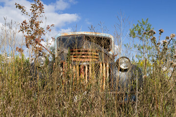 Close up front view of abandoned old pickup truck neglected and discarded in a field of tall weeds...