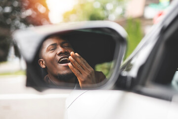 young black man with his new car look on mirror and yawn