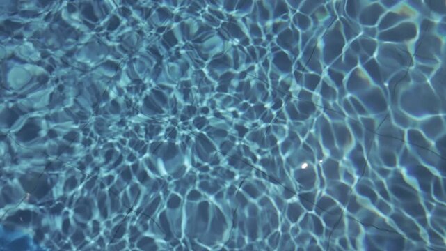 Continuously changing blue water of an outdoor swimming pool from above. Beautiful fresh wavy water surface on a sunny day. Calm and meditative vacation. Abstract slow motion for background.