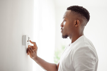 A Smiling black Man Adjusting Thermostat On Home Heating System