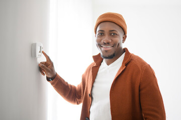 A Smiling black Man Adjusting Thermostat On Home Heating System