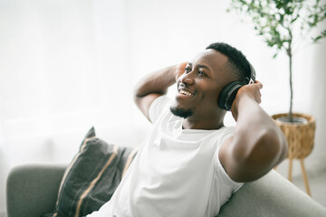 Fototapeta premium Cheerful black man using headphone on sofa.
