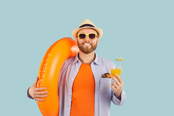 Fototapeta premium Smiling man in sunglasses and beachwear on summer vacation or weekend getaway, holding a cocktail and an inflatable ring. Beachside relaxation and travel adventures, radiating positivity and joy.