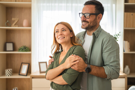 Happy couple embracing and looking away in living room