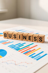 Fototapeta premium Wooden blocks spelling BUSINESS placed on office desk with printed charts and colorful graphs, symbolizing corporate growth, financial strategy, planning, analysis, and workplace productivity