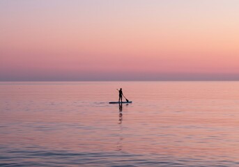 Solitary paddleboarder at dawn on calm sea.