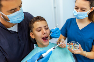 Two Dentists Treating Boy’s Teeth with Drill Extension in Clinic