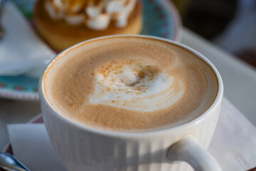 A creamy cappuccino with heart-shaped foam sits beside a tempting dessert in a cozy café setting.