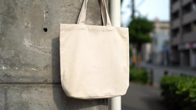 Blank Canvas Tote Bag Hanging on Urban Wall - A beige canvas tote bag hangs on a weathered concrete wall in an urban setting.