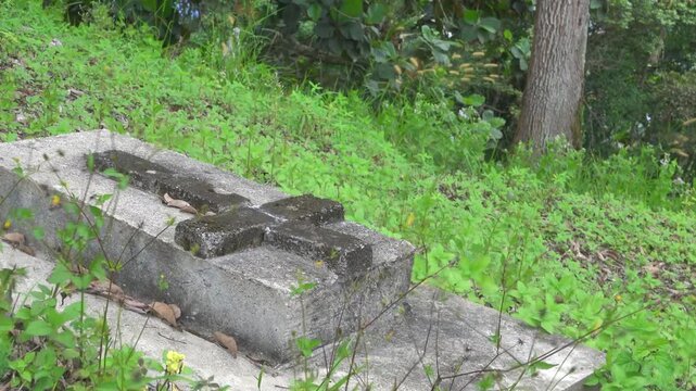 An unkempt grave in the forest with a stone cross. Malaysia traces of British colonialism on North Borneo