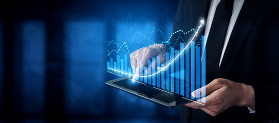 A businessman interacts with a tablet display showing financial graphs and data visualizations....