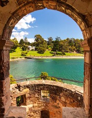 Naklejka premium A picturesque view of a harbor, framed by an ancient stone archway, showcases a serene coastal scene.