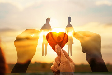 Hands holding paper figures with sunset background.